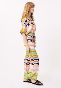 Tweedelig outfit bestaande uit een kortarmige, knoopjeshemd en losse broek. Gemaakt van kleurrijke stof met verschillende patronen en vormen.
