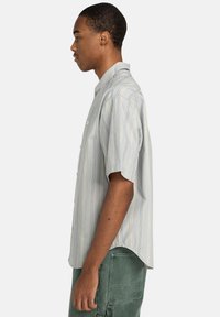 Short-sleeve button-up shirt in light blue with vertical yellow and navy stripes; features a classic collar and a relaxed fit design.