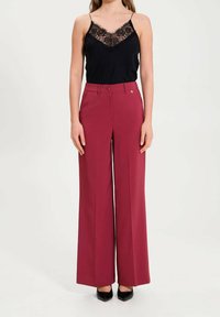 Maronfärgade vida byxor i lätt tyg med midjeband och knäppning. I kombination med en svart linne med spetsdetaljer.