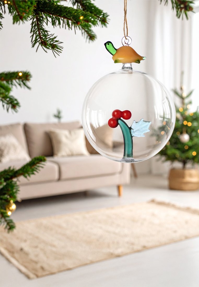 Przezroczysta szklana ozdoba choinkowa z zieloną gałązką ostrokrzewu, czerwonymi jagodami oraz przykrywką w kształcie żółwia. Zawieszona na naturalnej pętelce z juty.