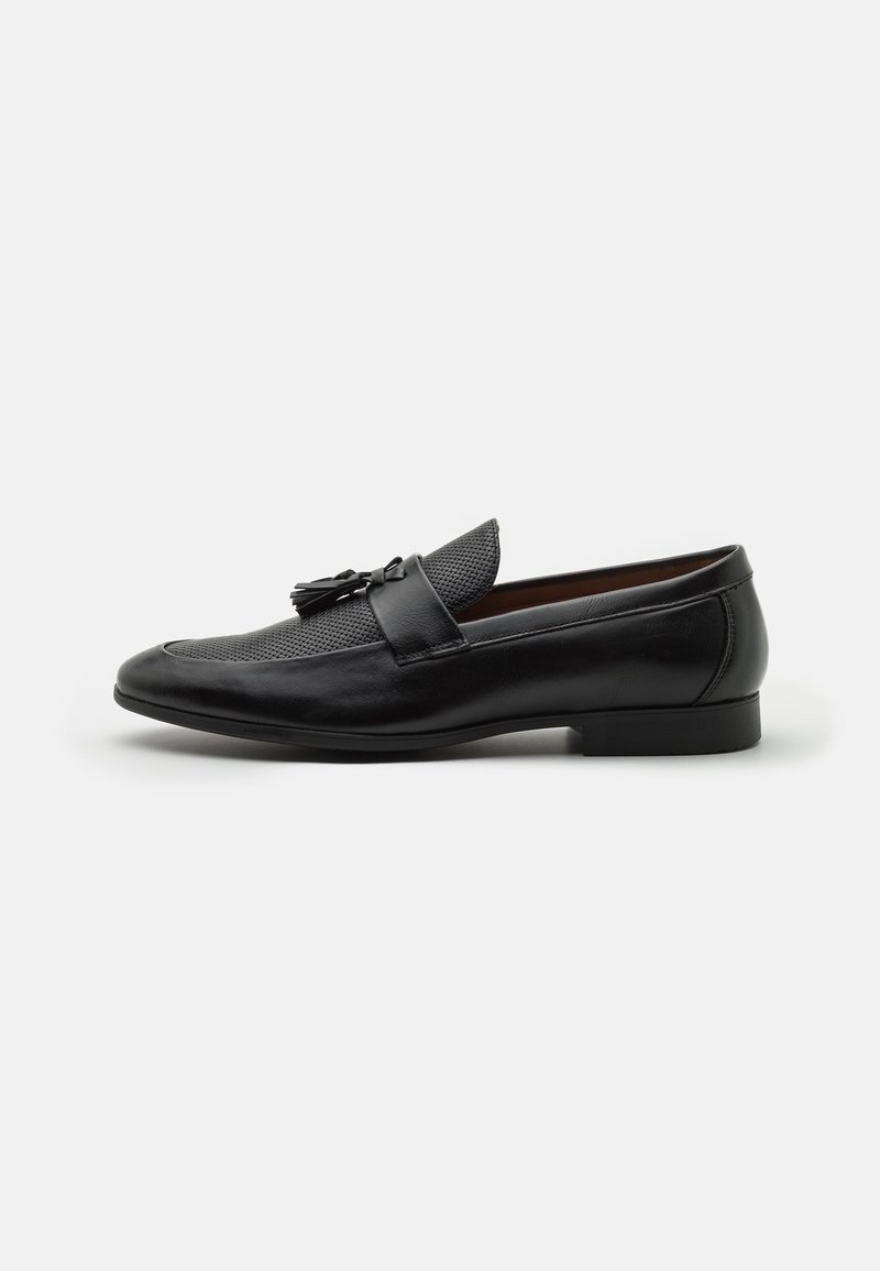 Mocassins en cuir noir avec un dessus en maille texturée, bout pointu, accents décoratifs de gland et un petit talon empilé.