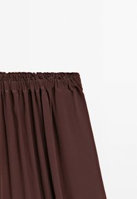 Jupe marron avec taille élastiquée froncée en tissu doux et léger, présentée sur un fond blanc uni.