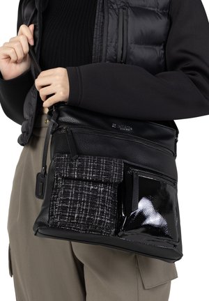 Sac en cuir noir avec une finition texturée, plusieurs sections à glissière et une poche en tissu à carreaux, agrémenté d'un accent noir brillant.
