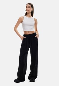 Schwarze weit geschnittene Hose mit lockerer Passform und elastischem Bund, kombiniert mit einem figurbetonten weißen kurzärmeligen Top aus Rippstoff. Glatte, leichte Stoffqualität.