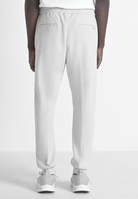 Pantalons de survêtement gris clair avec une taille élastique, coupe ajustée et deux poches arrière. Associés à des baskets grises, texture lisse.