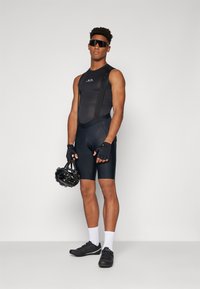 Svart sykkel-bibshorts med en tettsittende design, teksturert stoff og skulderstropper; kombinert med fingerløse hansker og en svart hjelm.