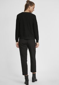 Pull en tricot noir avec des points en relief, encolure ronde et manches longues, porté avec un pantalon noir à coupe ajustée et des bottines.
