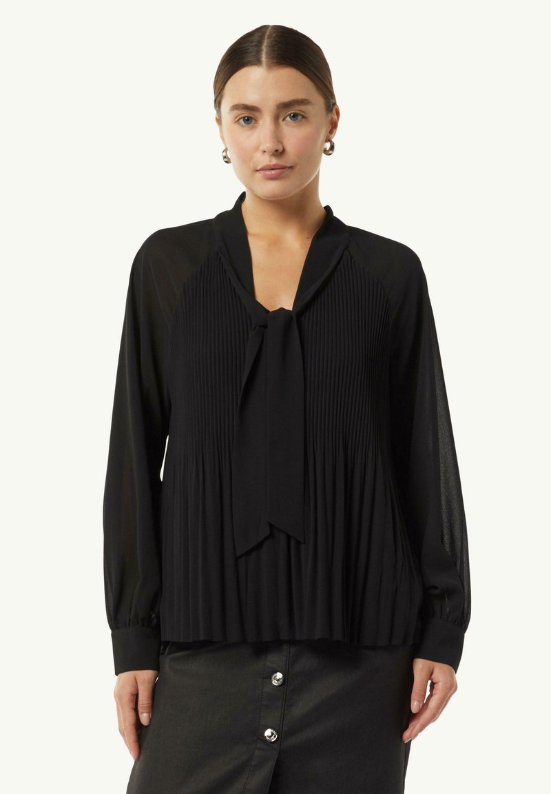 Schwarze Bluse mit Falten, einem Bindeband am Hals und langen Ärmeln. Weicher Stoff mit fließender Silhouette und leicht transparentem Textur.