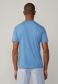 Světle modré bavlněné tričko s krátkými rukávy a kulatým výstřihem, s hladkou texturou a jednoduchým designem. Zobrazeno zezadu.