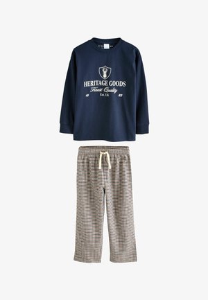 Chemise à manches longues bleue marine avec texte et logo blancs ; pantalons de pyjama à carreaux avec cordon de serrage dans des tons beige, bleu et marron. Tissu en coton doux.