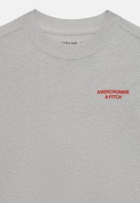 Sudadera gris hecha de material suave, con cuello redondo, mangas fijadas y un logo bordado rojo de "ABERCROMBIE & FITCH" en el pecho.