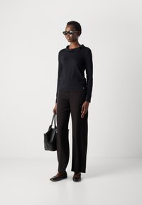 Zwarte longsleeve top met een ronde hals, gecombineerd met zwarte wijde broek. Accessoires zijn onder andere zwarte zonnebril en een gestructureerde zwarte handtas.