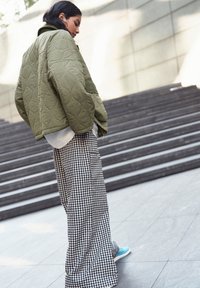 Veste matelassée vert olive, haut blanc et pantalon large en vichy noir et blanc. Des baskets bleues complètent la tenue. Des textures et motifs saisissants.