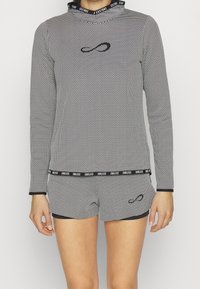 Langärmliges Oberteil mit Schwarz-Weiß-Muster und Kapuze, kombiniert mit passenden Shorts. Verfügt über ein Logo auf der Brust und einen gebrandeten Taillenbund. Dehnbare Stoffqualität.