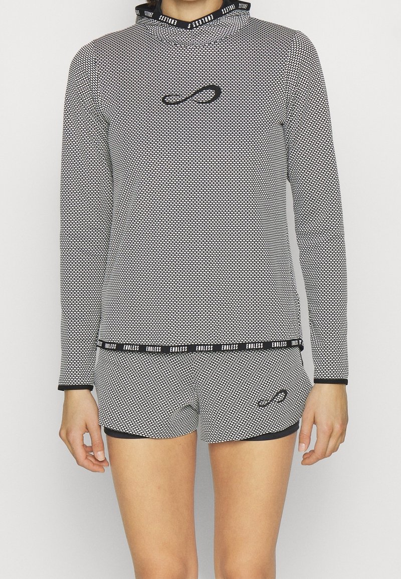 Langärmliges Oberteil mit Schwarz-Weiß-Muster und Kapuze, kombiniert mit passenden Shorts. Verfügt über ein Logo auf der Brust und einen gebrandeten Taillenbund. Dehnbare Stoffqualität.