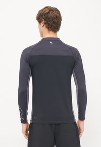 Długorękawowy rash guard w ciemnoszarym kolorze z purpurowymi akcentami. Posiada logo na górnej części pleców oraz dopasowany krój, idealny do aktywności wodnych.