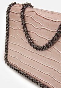 Vaaleanpunainen clutch-laukku krokotiilinjäljitelmällä ja kiiltävällä tummalla ketjuhihnalla valkoista taustaa vasten.