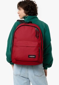 Červený batoh Eastpak s nastavitelnými popruhy, přední kapsou na zip a logem; vyrobený z odolné tkaniny, která má hladkou texturu.