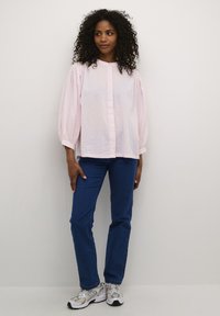 Light pink polka dot blouse with puffed sleeves, buttoned front, paired with blue straight-leg jeans and gray sneakers. White background.