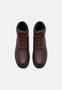 Botas de cuero marrón con un acabado texturizado, que presentan acentos negros, cordones marrones y una suela de goma, diseñadas para ofrecer durabilidad y soporte.
