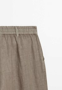 Pantalon en lin marron clair avec une texture, doté d'une taille élastique et de poches latérales, partiellement visible de la taille vers le bas.