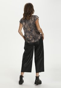 Blusa de manga corta con un patrón abstracto texturizado en tonos tierra. Combinada con pantalones de imitación cuero negros sueltos y botines negros.