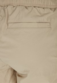 Tissu beige avec taille élastique et poche horizontale fendue cousue à l'arrière d'un pantalon ou d'un short.