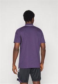 Lilla sports trøje med sorte sidepaneler og hvide detaljer, korte ærmer og krave. Bæres med sorte shorts.