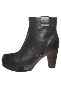 Bota de cuero negra hasta el tobillo con tacón alto. Presenta una punta redondeada, costuras visibles y pequeños acentos metálicos a lo largo de la suela.
