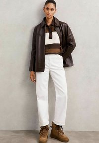 Brun læderjakke over en stribet sweater i brun og creme, parret med hvide bukser og brune snørebukser med furtrim.