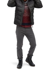 Giubbotto imbottito nero, maglione a maglia multicolore con rosso e blu, pantaloni grigi e stivali neri stringati con dettagli blu.