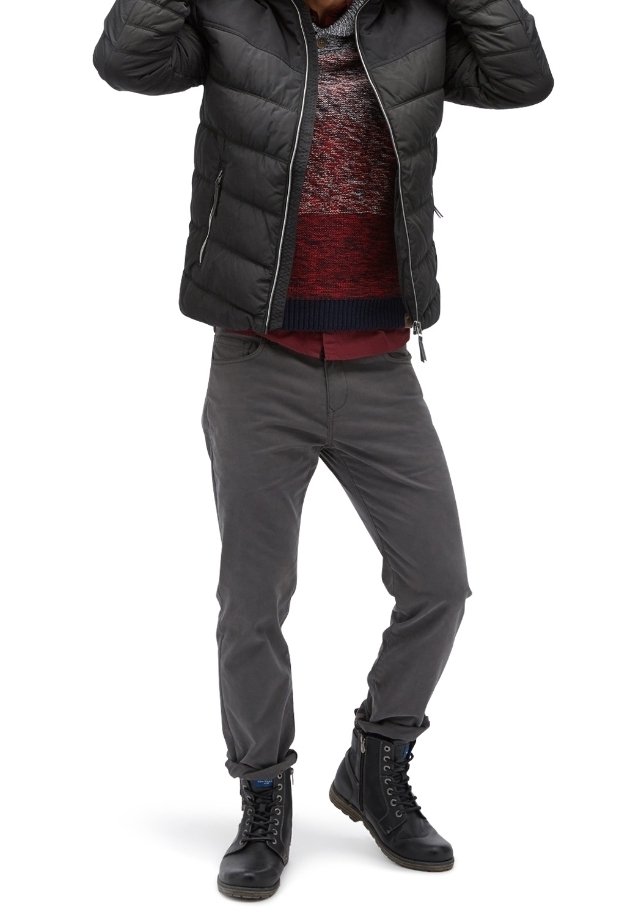 Giubbotto imbottito nero, maglione a maglia multicolore con rosso e blu, pantaloni grigi e stivali neri stringati con dettagli blu.