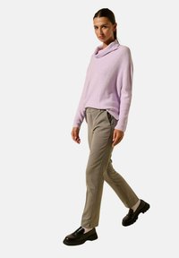 Pull en lilas clair à côtes avec un col drapé, associé à un pantalon gris clair à taille ajustée et des chaussures à semelle épaisse noires.