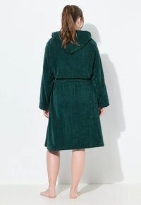 Accappatoio verde con cappuccio, realizzato in morbido tessuto spugna, con maniche lunghe, cintura in vita e orlo all'altezza del ginocchio.