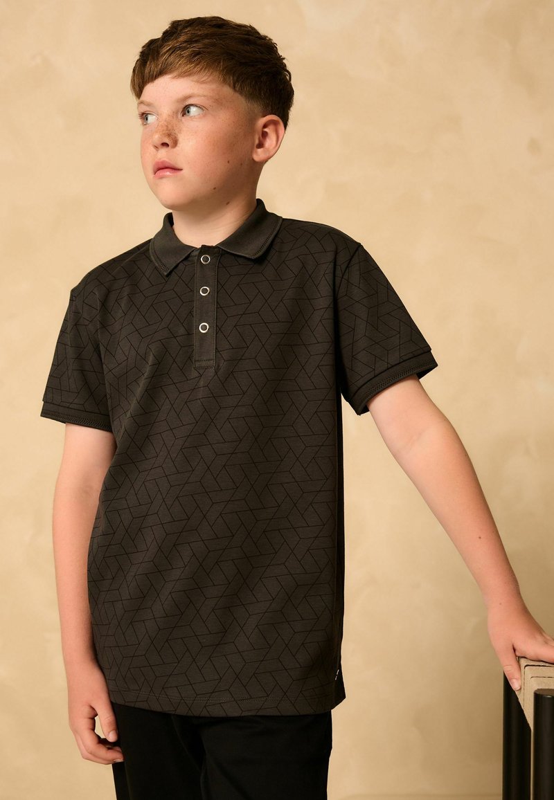 Short-sleeve, dark gray polo shirt with geometric pattern, three-button placket, and contrasting collar; paired with black trousers.