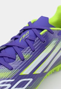 Purple soccer shoe with green accents, featuring a textured upper, flat laces, and the "F50" logo. Designed for performance with a sleek shape.