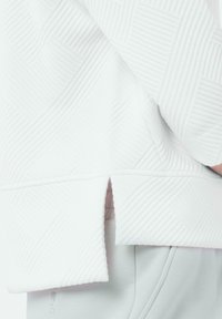 Witte sweatshirt met textuur en een geometrisch patroon, met een split-hem ontwerp. Zachte stof, relaxte pasvorm, met subtiele stikseldetails.