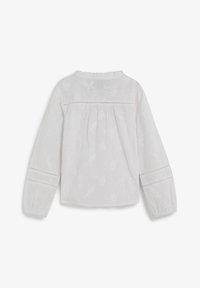 Blusa blanca de manga larga con un diseño texturizado, espalda fruncida y cuello con volantes, con patrones florales sutiles y puños elásticos.