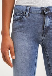 Jeans de mezclilla en un lavado azul desgastado, con un diseño clásico de cinco bolsillos, cierre de botón en el frente y una textura ligeramente desgastada.
