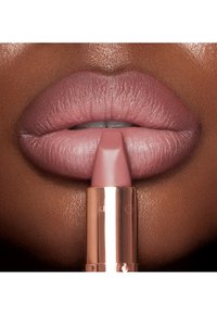 Lippenstift in einem rosé-nudefarbenen Farbton mit matter Oberfläche. Die Hülse hat eine rechteckige Form und wird nah an weichen, vollen Lippen gehalten. Die bronzefarbene Tube reflektiert das Licht.