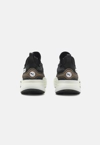 Schwarze Sportschuhe verfügen über ein strukturiertes Obermaterial, kontrastierende braune Akzente, ein weißes Logo und eine dicke, gepolsterte Sohle mit Grip-Mustern.