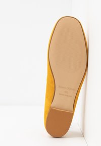 Zapato de ante amarillo con una suela texturizada y una base suave. Presenta un logotipo en relieve y una punta redondeada, diseñado para la comodidad y el estilo.