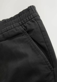 Black shorts made of smooth fabric, featuring a gathered elastic waistband and a slip pocket on the side.