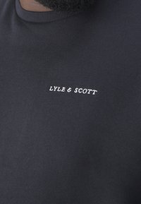 Černé bavlněné tričko s kulatým výstřihem, na hrudi s bílým vyšitým nápisem "LYLE & SCOTT". Hladký materiál, klasický střih.