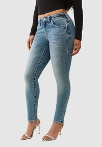 Jean skinny en denim bleu clair avec zones délavées, présentant un design classique à cinq poches et des détails en métal argenté.