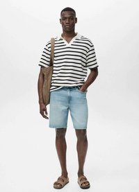 Tricou polo cu dungi alb-negru, cu mânecă scurtă, pantaloni scurți din denim bleu deschis, sandale maro și o geantă de umăr bej, plasate pe un fundal neutru.