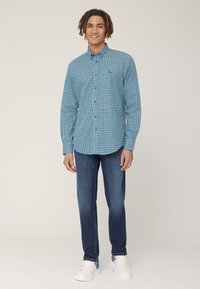 Camicia blu a righe con bottoni, maniche lunghe, taschino sul petto. Indossata con pantaloni in denim scuro e sneakers bianche. Design semplice con una vestibilità moderna.