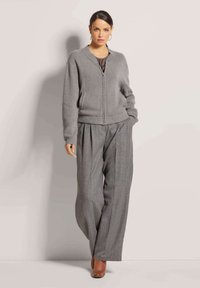 Graue gestrickte Bomberjacke mit gerippten Bündchen und Reißverschluss, kombiniert mit weit geschnittenen grauen gestreiften Hosen und braunen Stiefeletten.