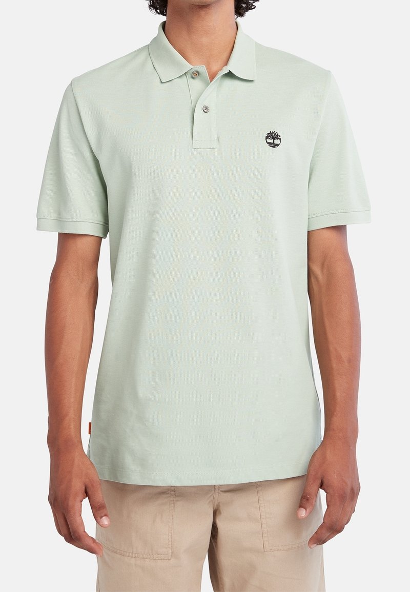 Polo vert clair à manches courtes, avec un col à deux boutons et un petit logo de marque sur la poitrine. Texture lisse et coupe décontractée.