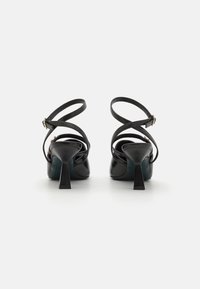 Svart høyhælte sandaler med kryssede ankelremmer, korte blokkerte hæler og en glatt lærfinish. Minimalistisk design med en strømlinjeformet silhuett.